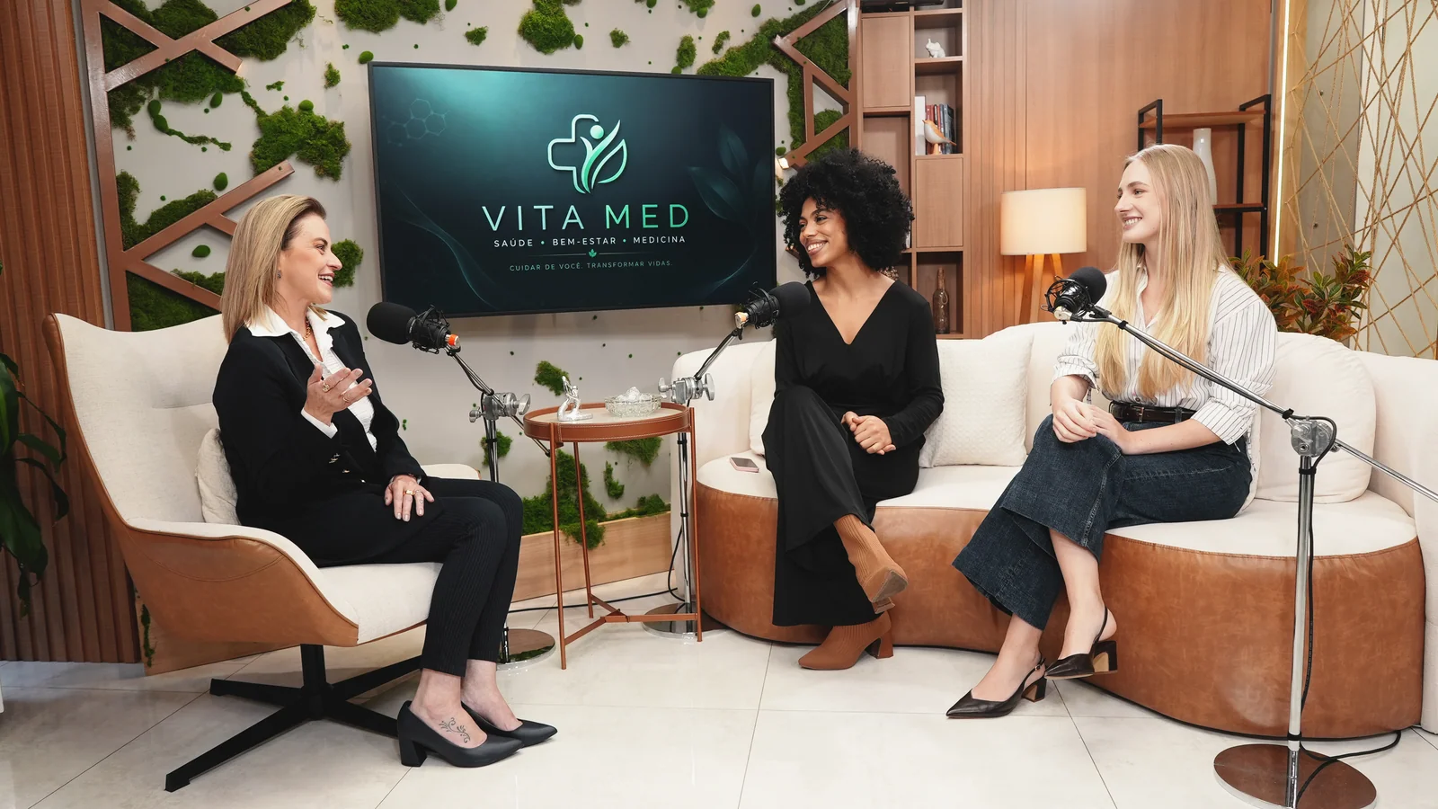 Living premium do Estúdio Master com sofá curvo branco, poltrona, TV de 55 polegadas e jardim de inverno durante uma gravação